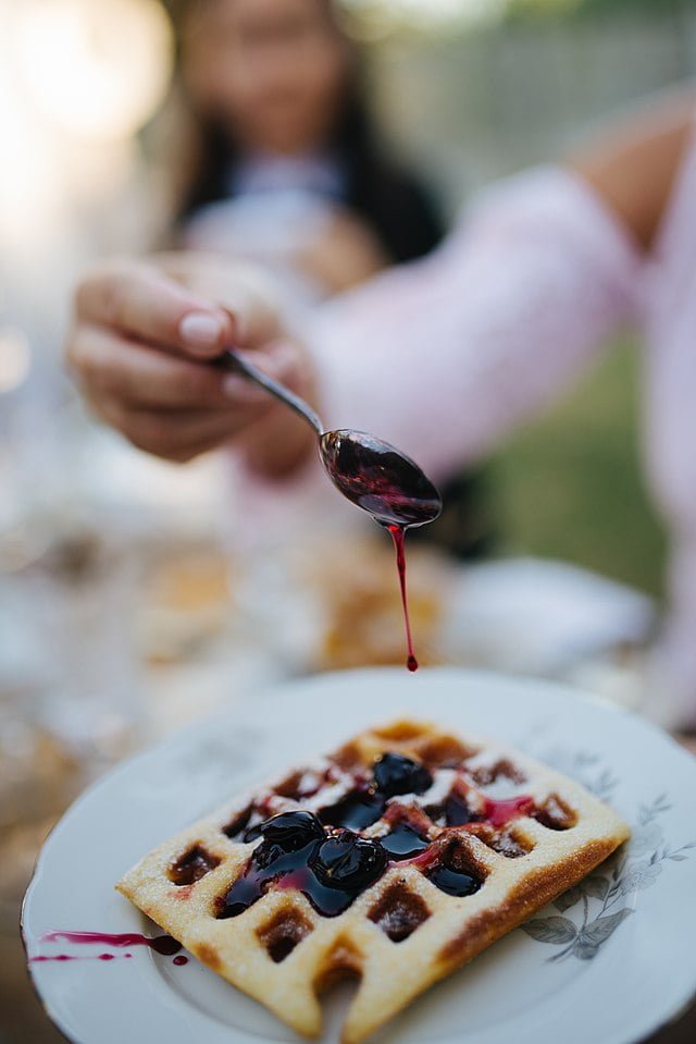 closeup of the woman putting blueberry syrup on the waffle 50345667573
