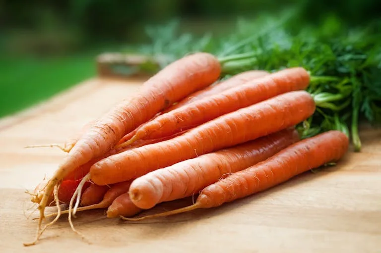 A bunch of fresh organic carrots on a wooden surface, perfect for healthy cooking.