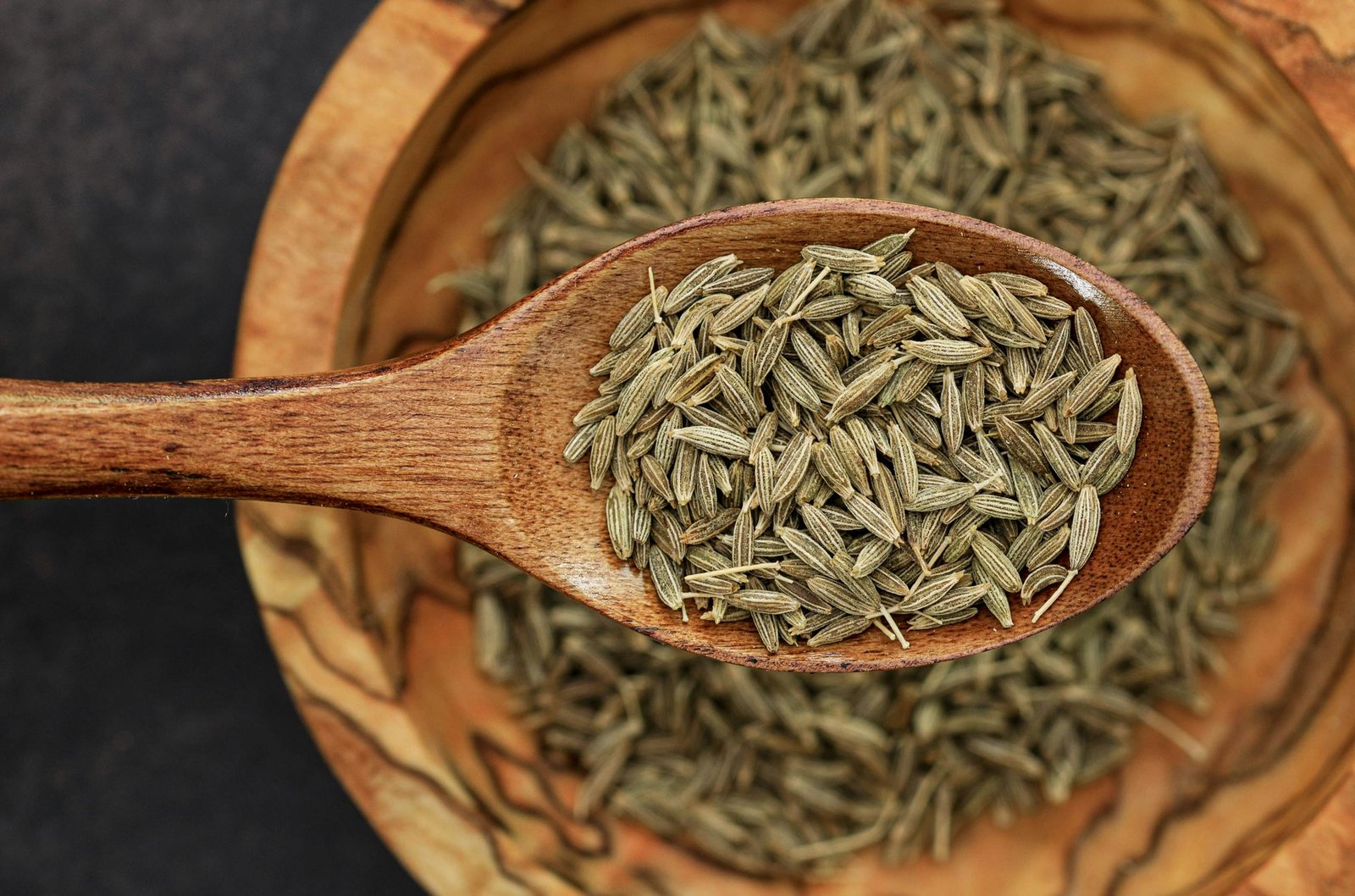 Detailed image of cumin seeds on a wooden spoon for culinary use.